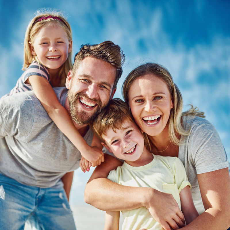 A joyful family of four, including a daughter and a son, smiling and laughing together, showcasing the connection between gratitude and happiness.