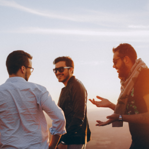 Three friends laughing and enjoying a conversation at sunset, symbolizing connection, openness, love, and understanding.