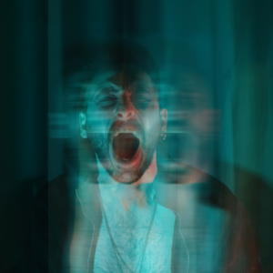 A distressed man screams with his mouth wide open, surrounded by motion blur, creating a ghostly, fragmented effect—symbolizing emotional overwhelm and the isolating intensity of anger he feels.