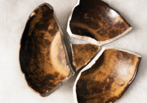 A broken ceramic bowl with its pieces laid out on a soft surface, symbolizing the concept of breaking open rather than being broken.