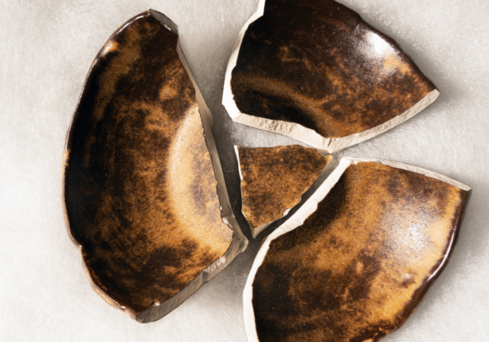 A broken ceramic bowl with its pieces laid out on a soft surface, symbolizing the concept of breaking open rather than being broken.