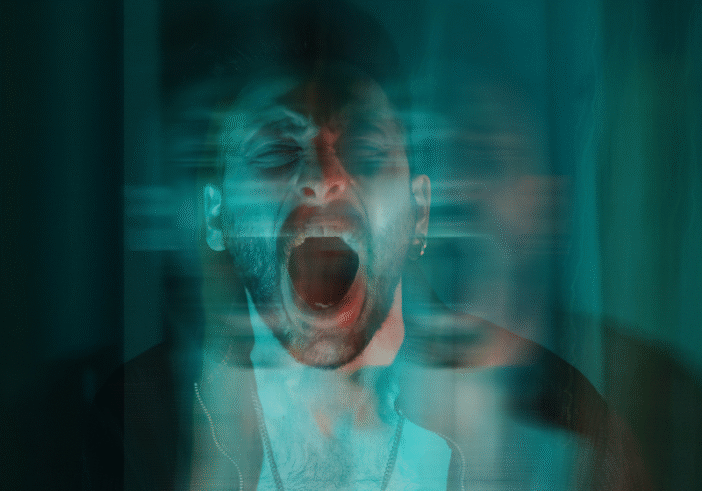 A distressed man screams with his mouth wide open, surrounded by motion blur, creating a ghostly, fragmented effect—symbolizing emotional overwhelm and the isolating intensity of anger he feels.