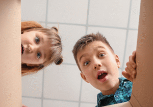 Two curious children looking into a cardboard box with expressions of wonder, uncertainty and surprise, symbolizing the excitement and creativity that arise from the unknown.