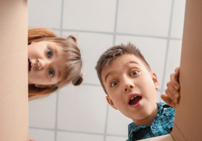 Two curious children looking into a cardboard box with expressions of wonder, uncertainty and surprise, symbolizing the excitement and creativity that arise from the unknown.