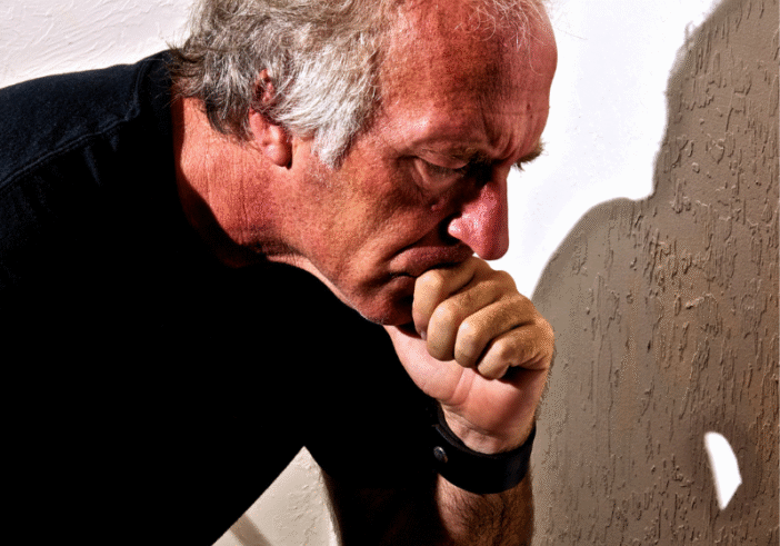 An older man deep in thought, resting his chin on his hand, with a solemn expression and a shadow cast on the wall behind him, reflecting the weight of pain.