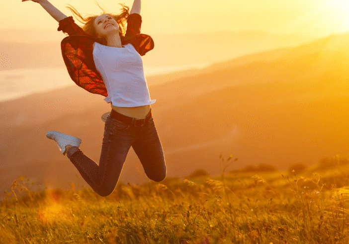 A woman jumping joyfully in front of a mountainous landscape, capturing the sense of freedom, gratitude, and happiness.