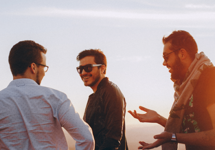 Three friends laughing and enjoying a conversation at sunset, symbolizing connection, openness, love, and understanding.